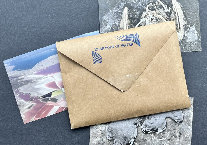 An envelope with a stamp on the back "Dear Body of Water" beneath the envelope are three partially obscured postcards