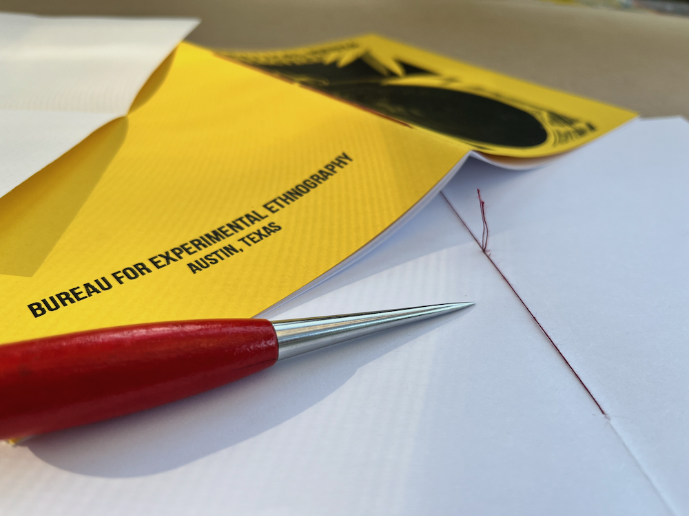 A pamphlet bound booklet with a yellow cover. An awl lying across a page with some red thread poking up.