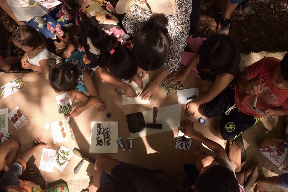 Photographic image looking down on a group of people. Their hands are visible and they are working with paper and crafts.